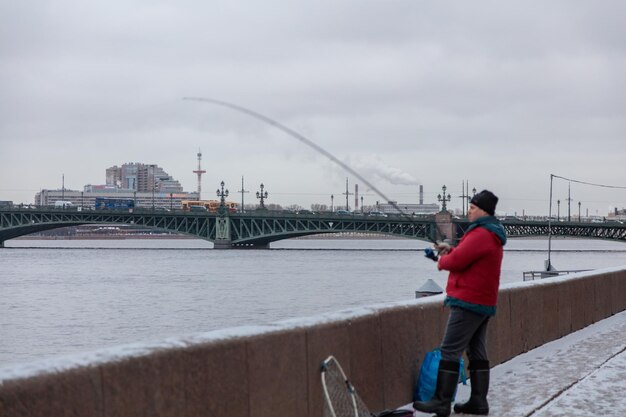 Photo un homme en veste rouge pêche dans l'eau avec un pont en arrière-plan.