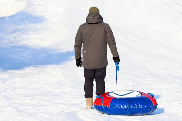 Un homme en vêtements chauds se tient au bas d'un toboggan à neige avec un tube rouge et bleu