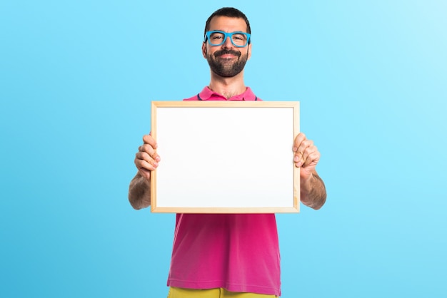 Homme avec des vêtements colorés tenant une affiche vide sur fond coloré