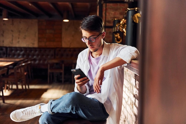 Homme en vêtements décontractés assis dans le pub avec téléphone à la main