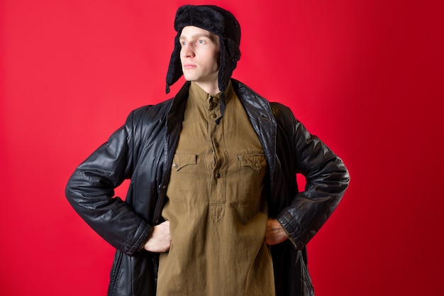 Un homme en vêtements démodés et un chapeau avec des oreillettes, style russe d'après-guerre.