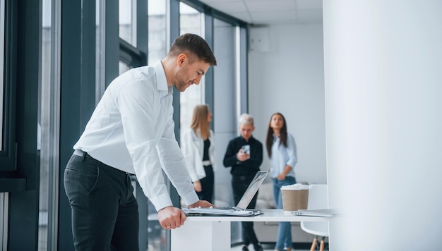 Homme en vêtements formels debout et lisant des documents devant une jeune équipe réussie qui travaille et communique ensemble à l'intérieur au bureau