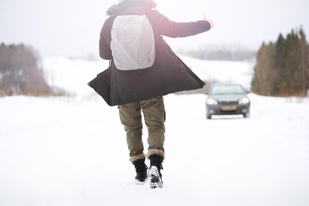 Un homme en vêtements d'hiver dans la rue. Les touristes voyagent à travers le pays enneigé. Sur le chemin, marchez et faites de l'auto-stop.