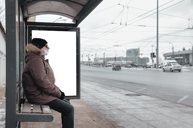 Photo homme en vêtements d'hiver décontractés avec lunettes et masque médical à l'arrêt de bus