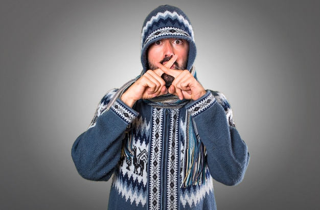 Homme avec des vêtements d&#39;hiver faisant un geste de silence sur fond gris