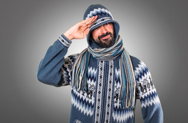 Un homme avec des vêtements d&#39;hiver saluant sur fond gris