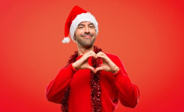 Homme avec des vêtements rouges, célébrant les vacances de Noël, faisant le symbole du coeur à la main