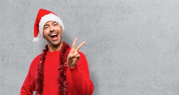 Homme avec des vêtements rouges célébrant les vacances de Noël en souriant et en montrant le signe de la victoire