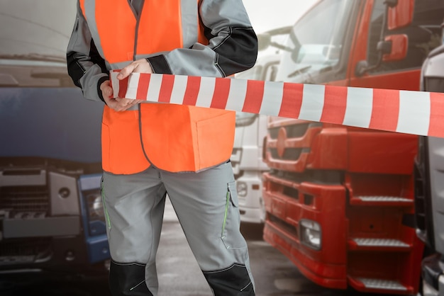 Un homme en vêtements spéciaux bloque le parking avec une bande de différents semi-remorques sur le fond