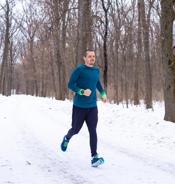 Homme en vêtements de sport bleu courant dans la forêt en hiver