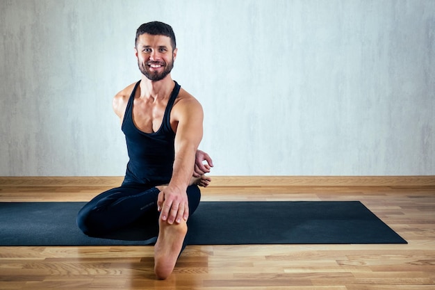 Un homme en vêtements de sport sombres pratiquant le yoga sur fond sombre. asana sur le sol sur des tapis de yoga. le concept de concentration et de possession du corps