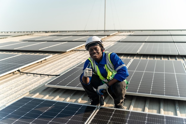 Un homme vêtu d'une chemise bleue et d'un casque de sécurité jaune est accroupi sur le toit d'un immeuble doté de panneaux solaires.