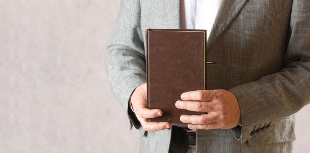 Un homme vêtu d'un costume classique tient un livre brun. Fermer