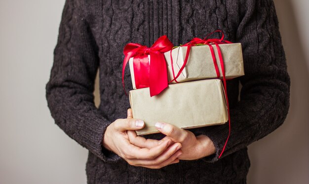 Un homme vêtu d'un pull gris foncé tient une boîte-cadeau avec un ruban rouge