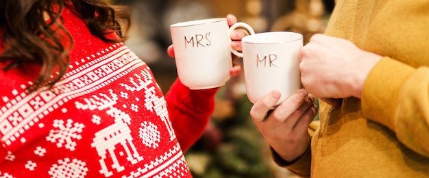 Un homme vêtu d'un pull jaune et une femme vêtue d'un pull rouge tiennent des tasses avec les mots M. et Mme. Ambiance romantique du Nouvel An. photo
