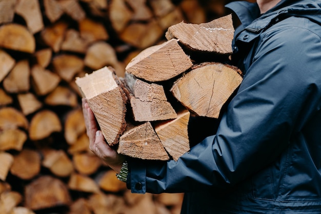 Un homme vêtu d'une veste porte un paquet de bois de chauffage