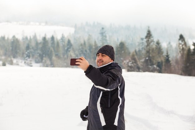 L'homme vêtu de vêtements chauds se tient avec un smartphone sur une colline enneigée