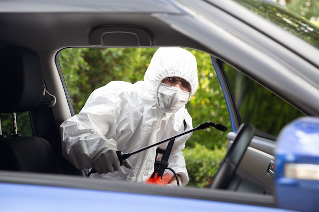 Un homme virologue portant des kits EPI tue les bactéries et les virus à l'intérieur de la voiture Service de stérilisation et de nettoyage COVID dans le concept de voiture