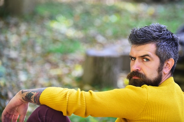 Homme avec le visage de ________ sur un bâtiment blanc / arrière-plan extérieur. Concept de détente et de temps d'automne. / Heure d'automne et concept de temps ensoleillé. Guy avec barbe se trouve sur la main courante en bois. Macho passe du temps dans