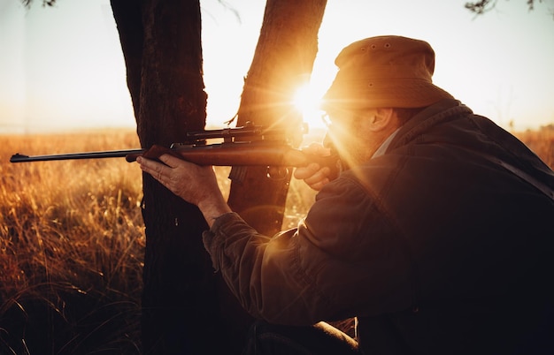 Un homme visant un fusil par le tronc d'un arbre sur le champ