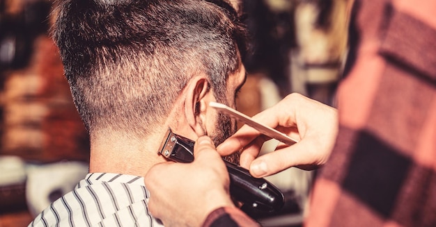 Homme visitant un coiffeur dans un salon de coiffure Le coiffeur travaille avec une tondeuse à cheveux Client hipster se fait couper les cheveux Mains de coiffeur avec une tondeuse à cheveux se bouchent Concept de coupe de cheveux