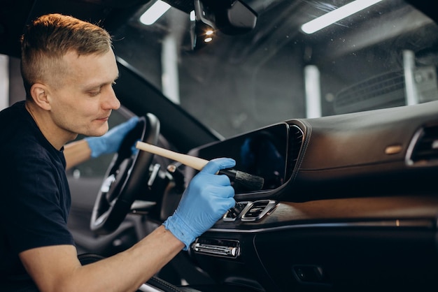 L'homme à la voiture nettoie à l'aide d'une brosse pour nettoyer tous les détails à l'intérieur du véhicule