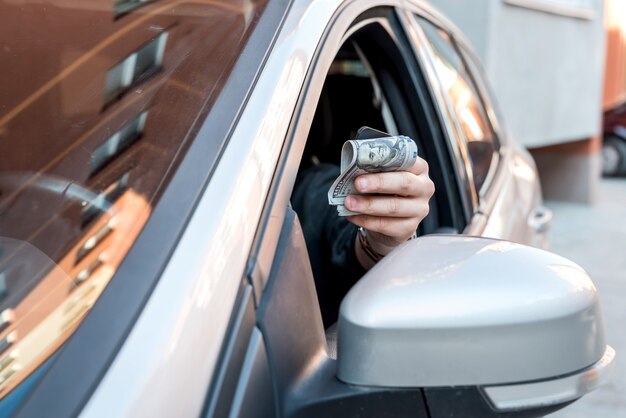 Homme en voiture tenant un dollar pour pot-de-vin ou payer en marchandises. concept de finance d'entreprise