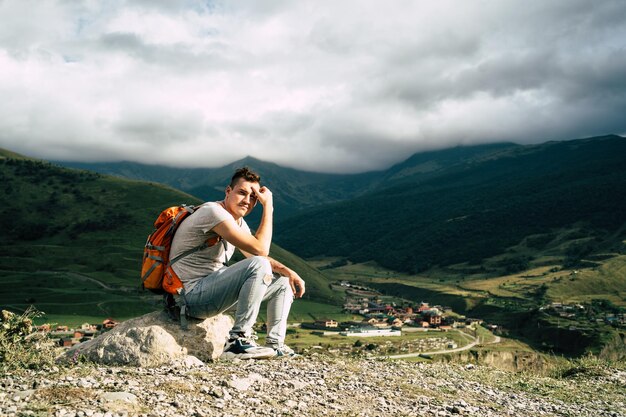 Homme de voyage fatigué reposant sur la colline Touriste masculin épuisé assis sur la pierre après une randonnée active dans les montagnes