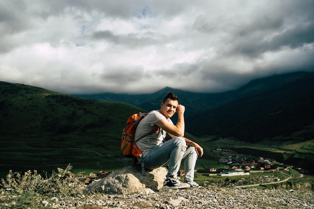 Homme de voyage fatigué reposant sur la colline Touriste masculin épuisé assis sur la pierre après une randonnée active dans les montagnes