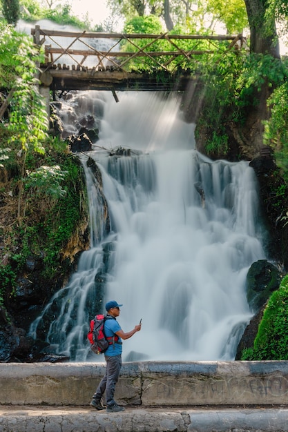 Un homme de voyage avec un téléphone portable prend une photo de la cascade