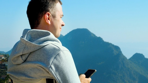 Homme de voyage avec téléphone portable en sweat à capuche assis et profiter de la vue sur la montagne