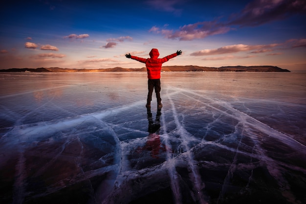 Homme De Voyageur Porter Des Vêtements Rouges Et Lever Le Bras Debout Sur La Glace Naturelle Dans L'eau Gelée Au Lac Baïkal, En Sibérie, En Russie.