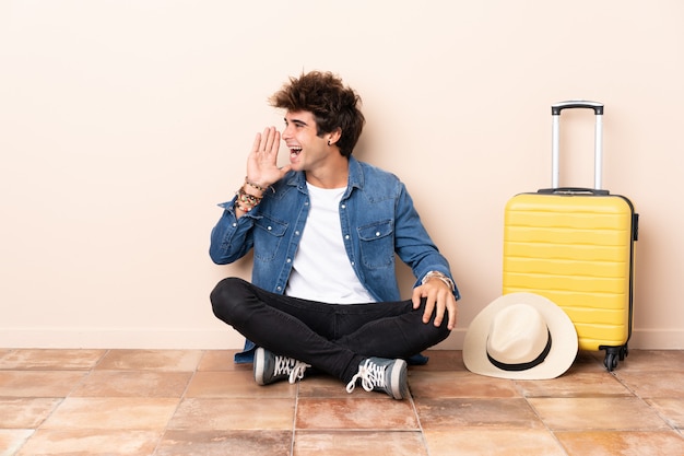 Photo homme voyageur sa valise assis sur le sol en criant avec la bouche grande ouverte