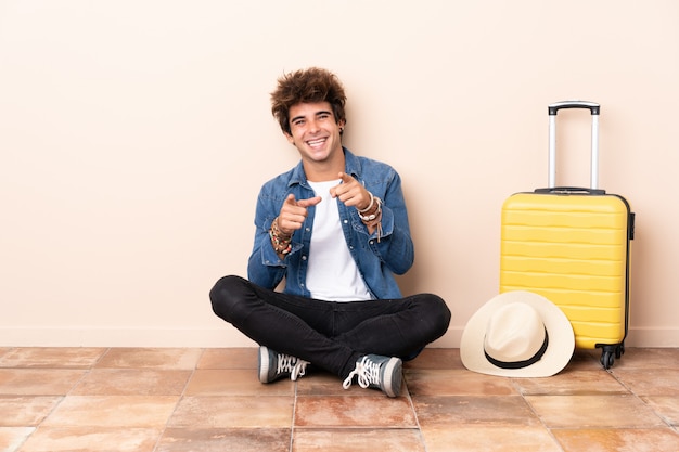 Homme voyageur sa valise assise sur le sol pointe le doigt vers vous