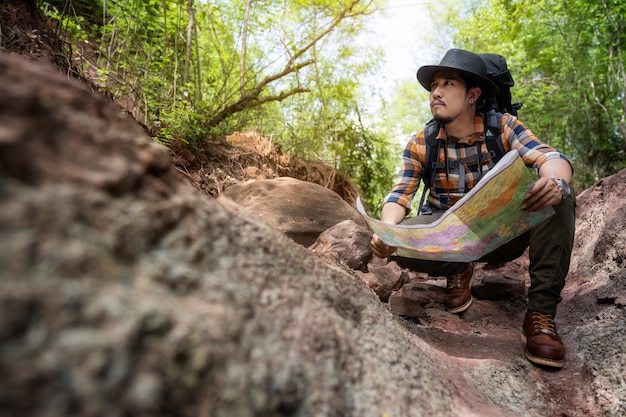 Homme voyageur avec sac à dos assis et lecture de carte dans la forêt