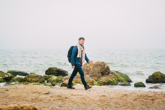 Homme de voyageur avec sac à dos debout sur une plage de sable au milieu des rochers sur fond de mer