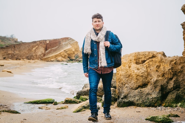 Homme de voyageur avec sac à dos debout sur une plage de sable au milieu des rochers sur fond de mer