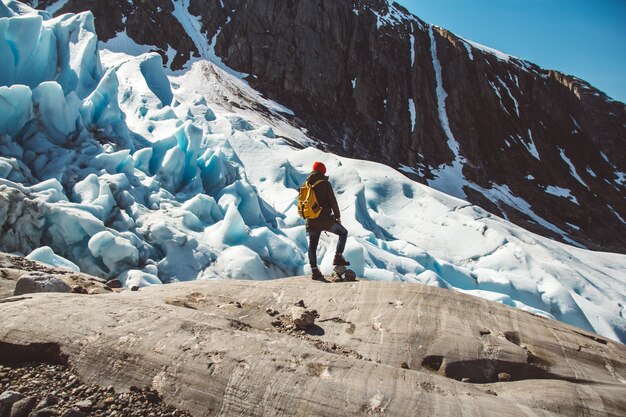 Homme de voyageur avec un sac à dos debout sur un rocher sur fond de montagnes glaciaires et de neige