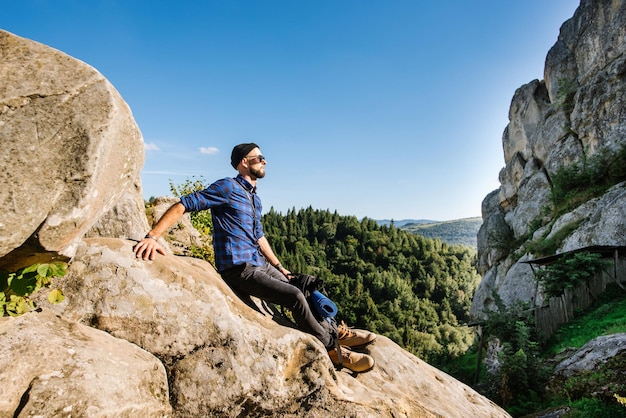 Un homme voyageur avec sac à dos et lunettes de soleil assis sur les rochers à la montagne