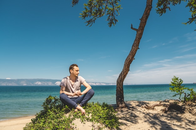 Homme voyageur se détendre sur la plage de l&#39;île d&#39;Olkhon surplombant l&#39;eau du lac et les montagnes et le ciel bleu