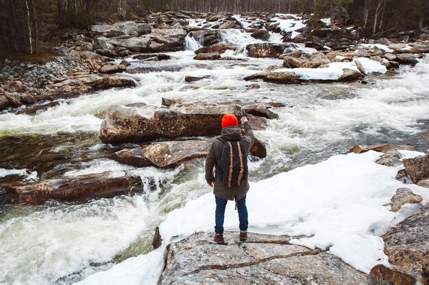 Homme de voyageur tenant une boussole sur fond de rochers de rivière de montagne et de forêt