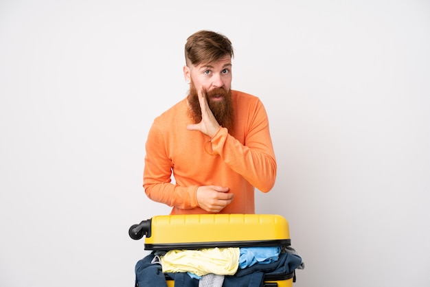 Homme voyageur avec une valise pleine de vêtements sur mur blanc isolé chuchoter quelque chose