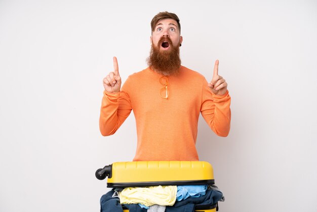 Homme voyageur avec une valise pleine de vêtements sur un mur blanc isolé pointant avec l'index une excellente idée