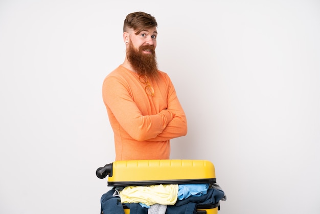 Homme voyageur avec une valise pleine de vêtements sur un mur blanc isolé en riant