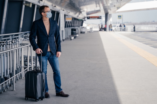 Homme voyageur avec valise porte un masque de protection