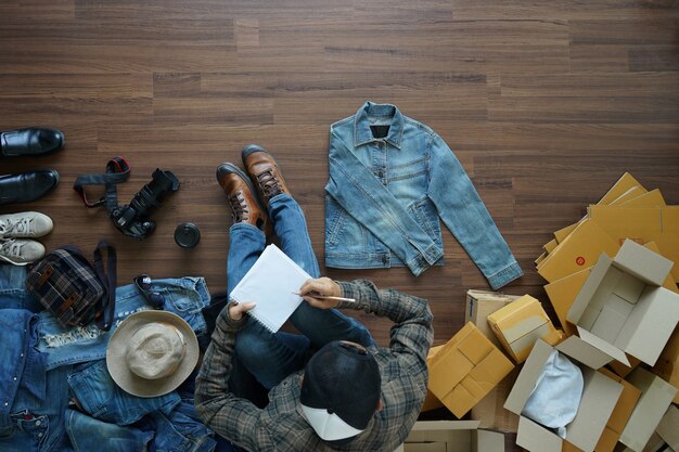 Homme vue de dessus, assis sur un plancher en bois et écrit dans le carnet de notes