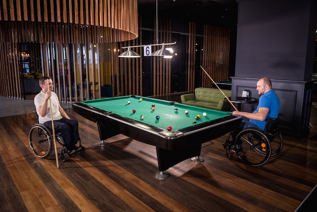 Les hommes adultes handicapés dans un fauteuil roulant jouent au billard dans le club