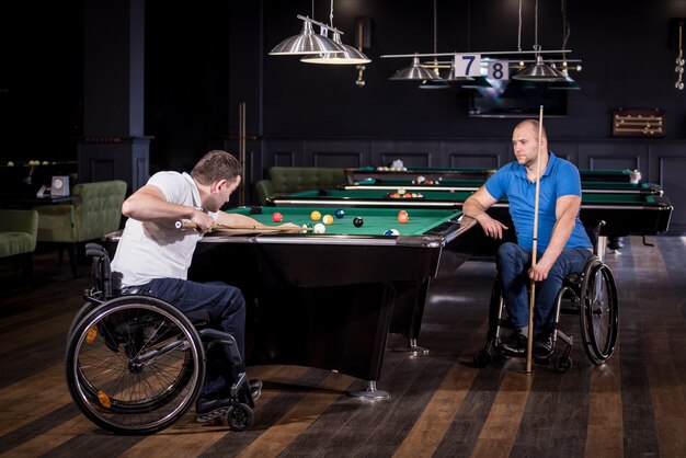 Des hommes adultes handicapés en fauteuil roulant jouent au billard dans le club