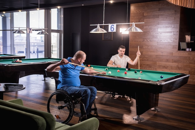 Des hommes adultes handicapés en fauteuil roulant jouent au billard dans le club