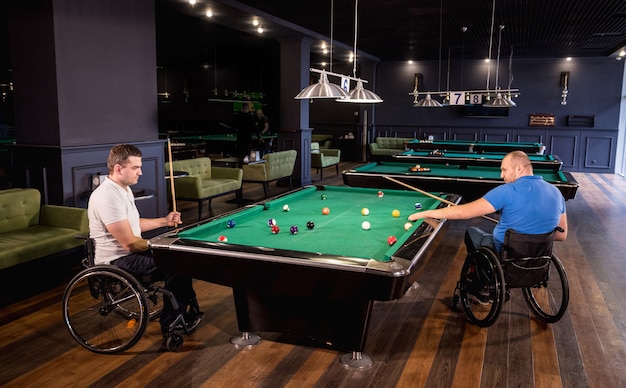 Des hommes adultes handicapés en fauteuil roulant jouent au billard dans le club